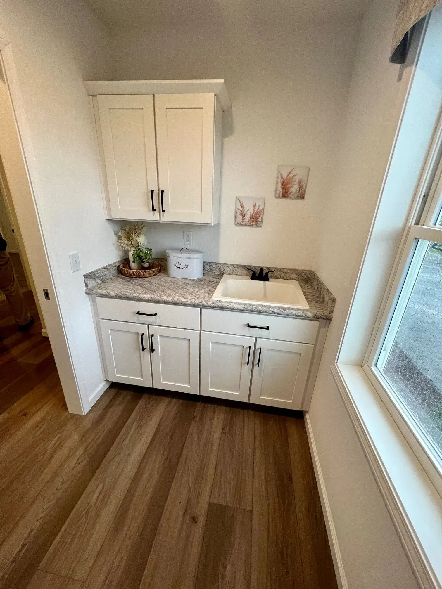 Laundry room with white cabinets, a sink, window, and wood-look flooring.