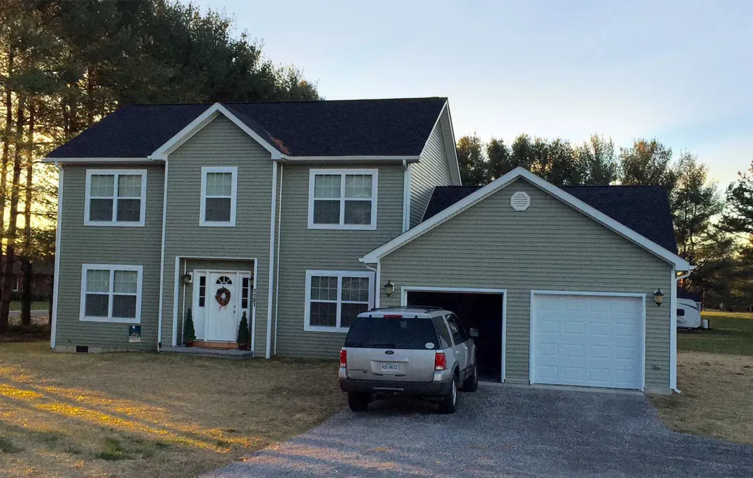 Two-story house with attached garage. Green siding, white trim, dark roof. A car sits in the driveway.