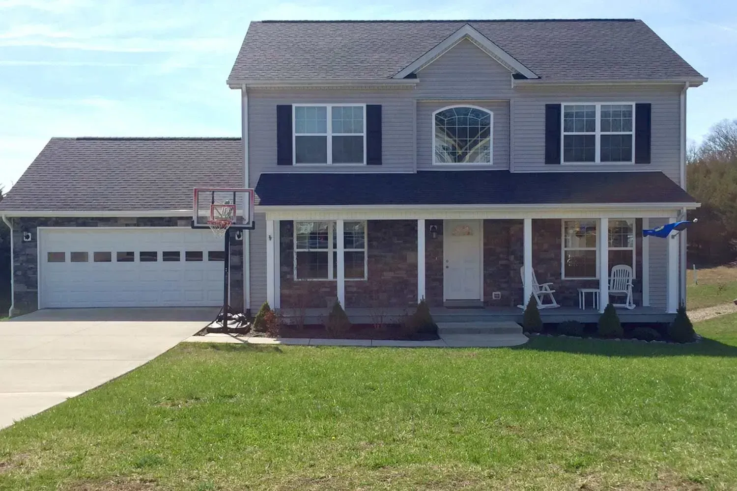 Two-story house with gray siding, attached garage, and a covered porch. A basketball hoop is in the driveway.