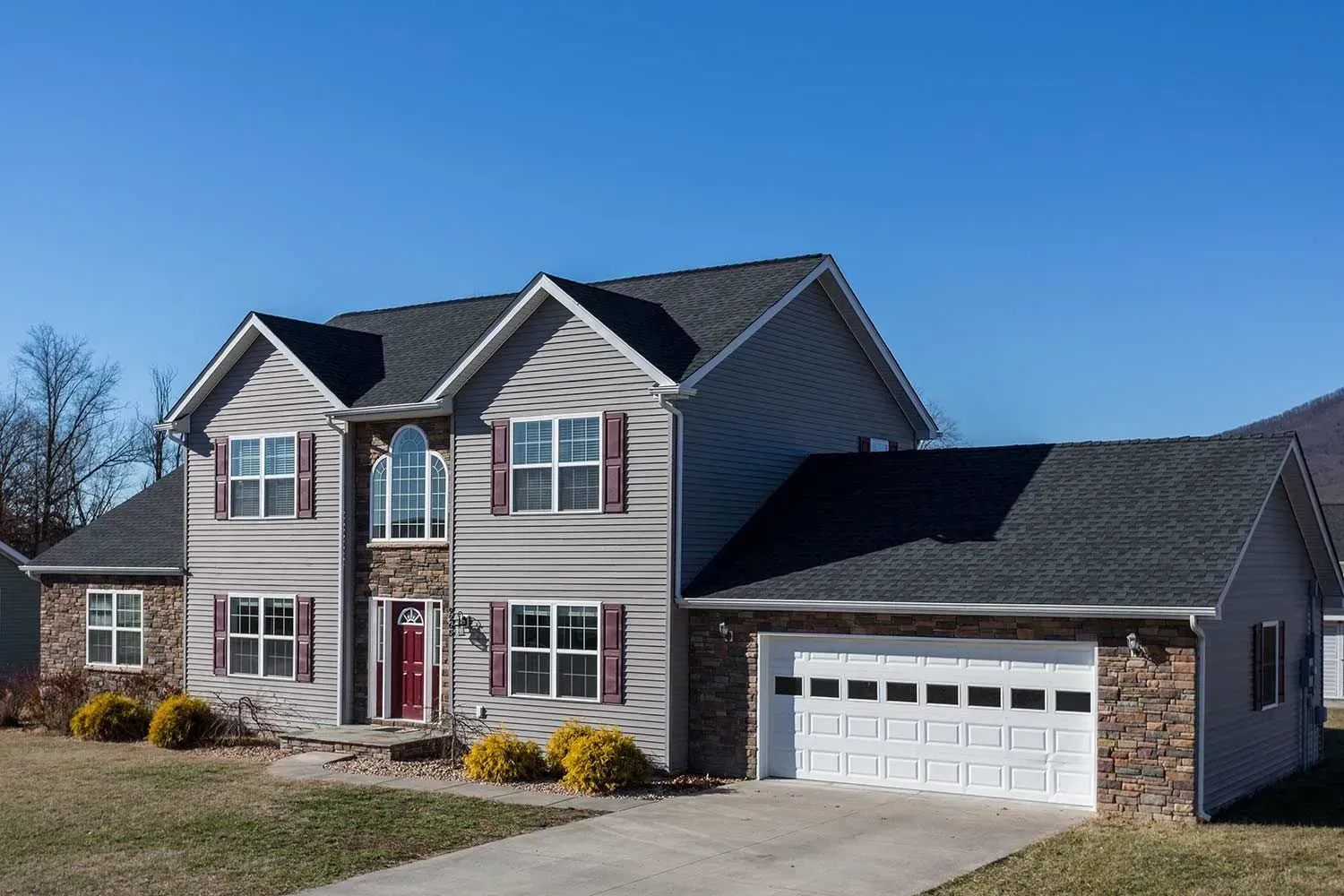 Two-story house with gray siding, a garage, and a driveway, under a clear blue sky.