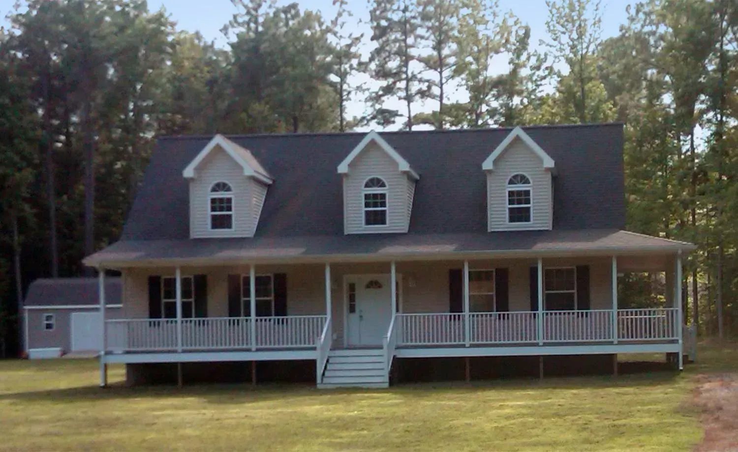 Beige house with a wraparound porch, three dormers, and a small shed.