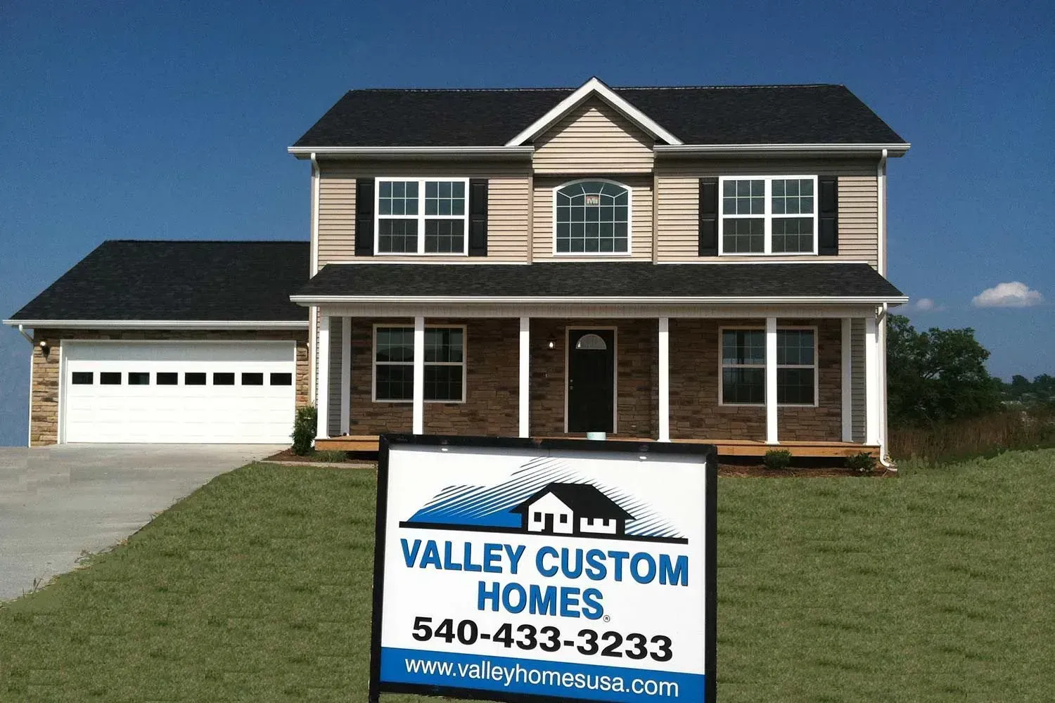 Two-story house with black roof, beige siding, and a sign that reads 