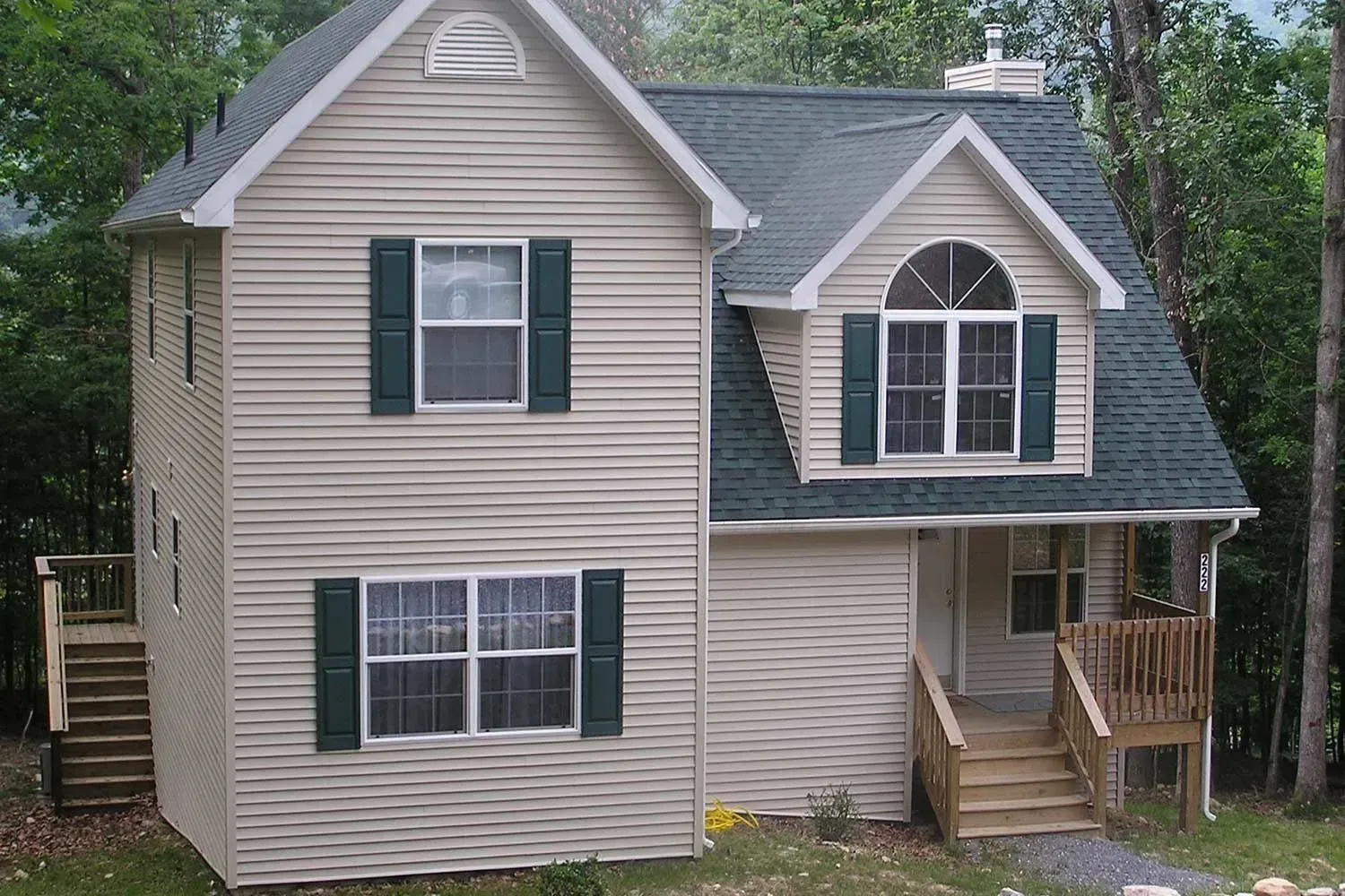 Two-story house with green shutters, green roof, and wooden stairs leading to the entrance and a side deck.