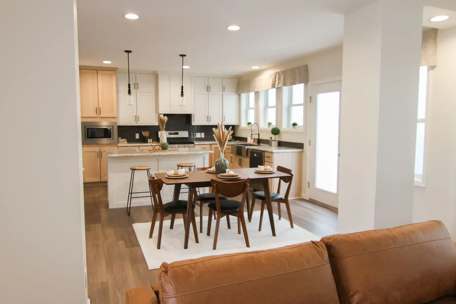 Open-concept kitchen and dining area with light wood cabinets, dark dining table and chairs, and a light-colored rug.