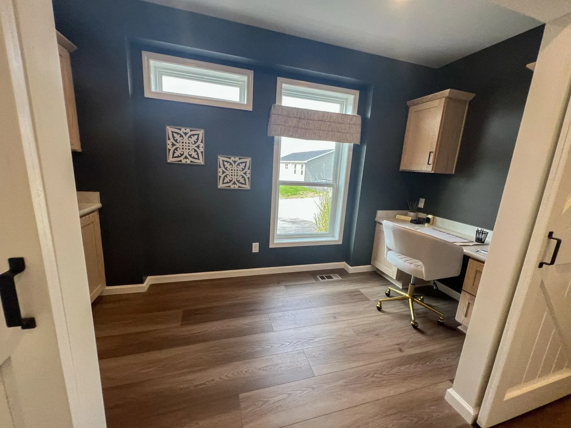 A home office with dark gray walls, light wood-look flooring, desk, and windows.