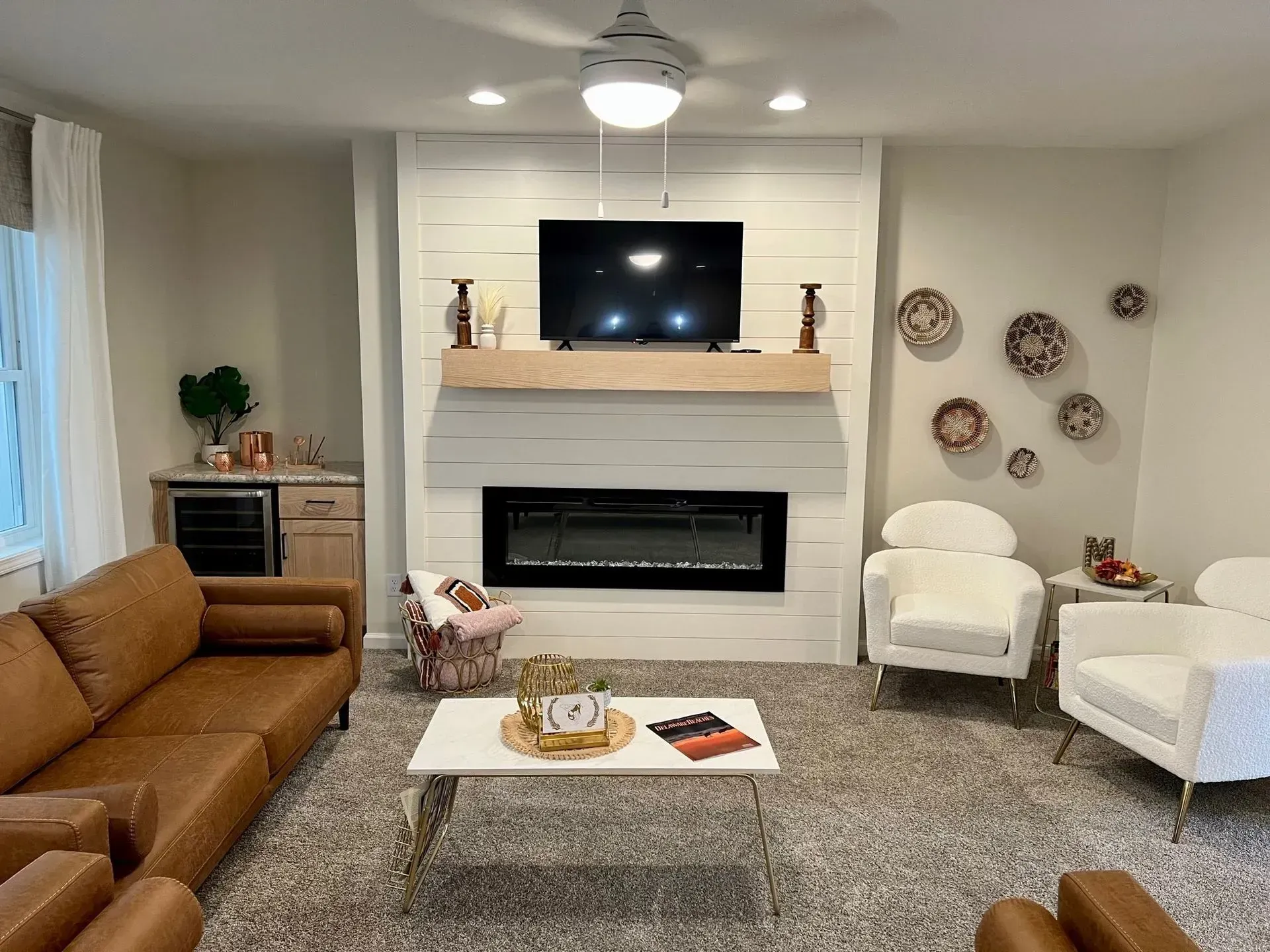 Living room with white fireplace, TV, brown sofa, white chairs, and decorative wall plates.