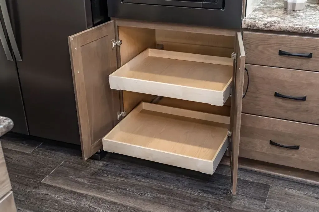 Open kitchen cabinet with two pull-out shelves; wooden, light-colored interior, dark handles, and countertop.