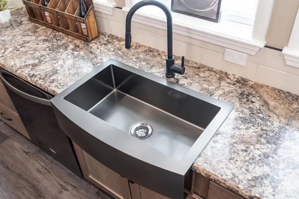 Stainless steel farmhouse sink in kitchen with black faucet.