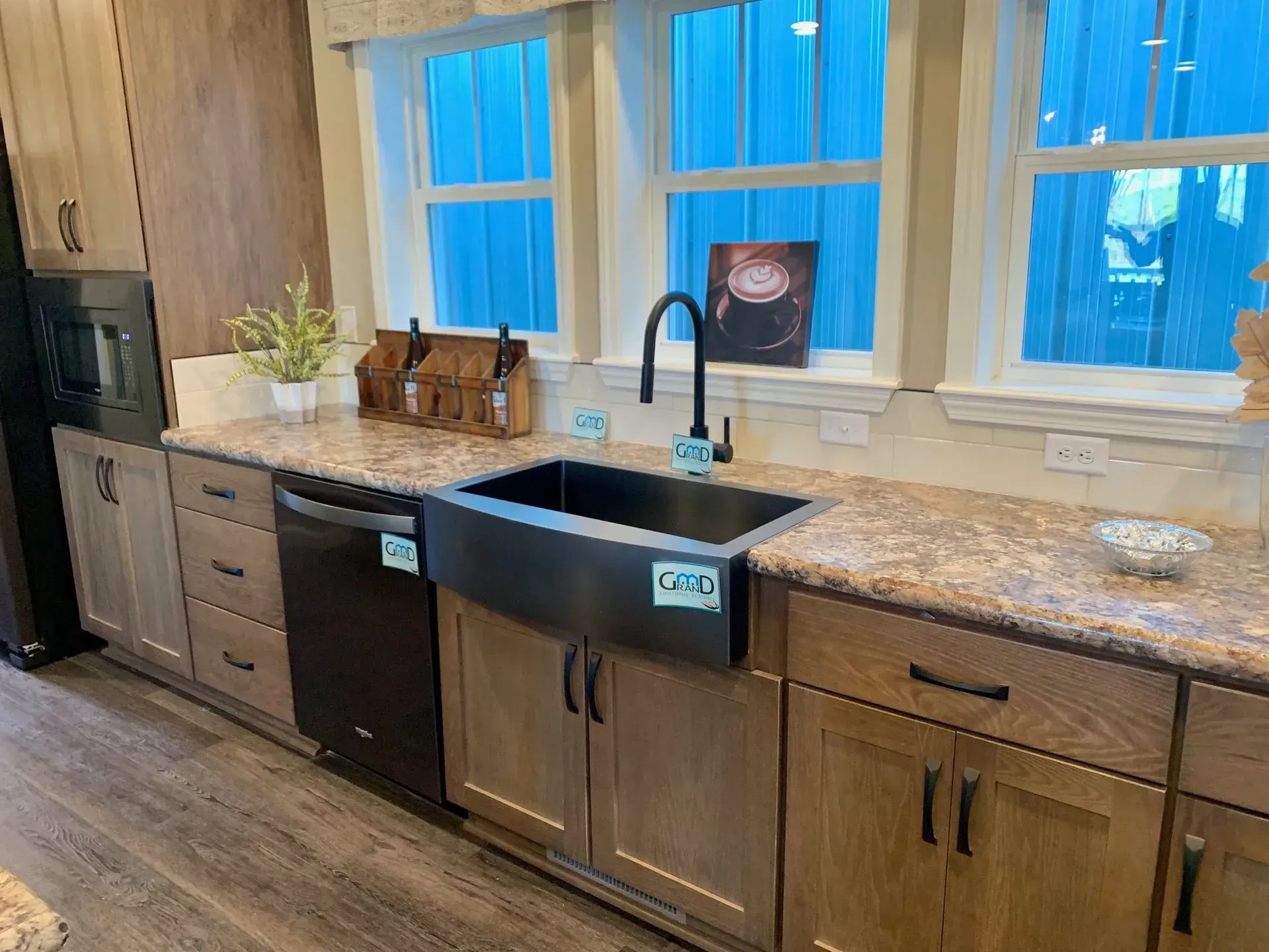 Kitchen with stainless steel sink, black faucet, brown cabinets, and a dishwasher, under a window.