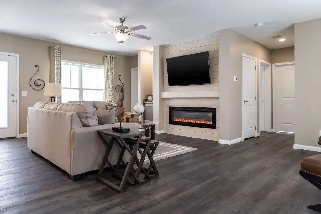 Living room with sofa, fireplace, and TV on a light brown wall, dark wood floors.