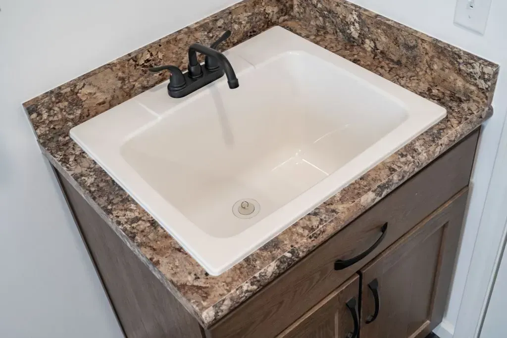 White utility sink with black faucet on brown countertop and cabinet.