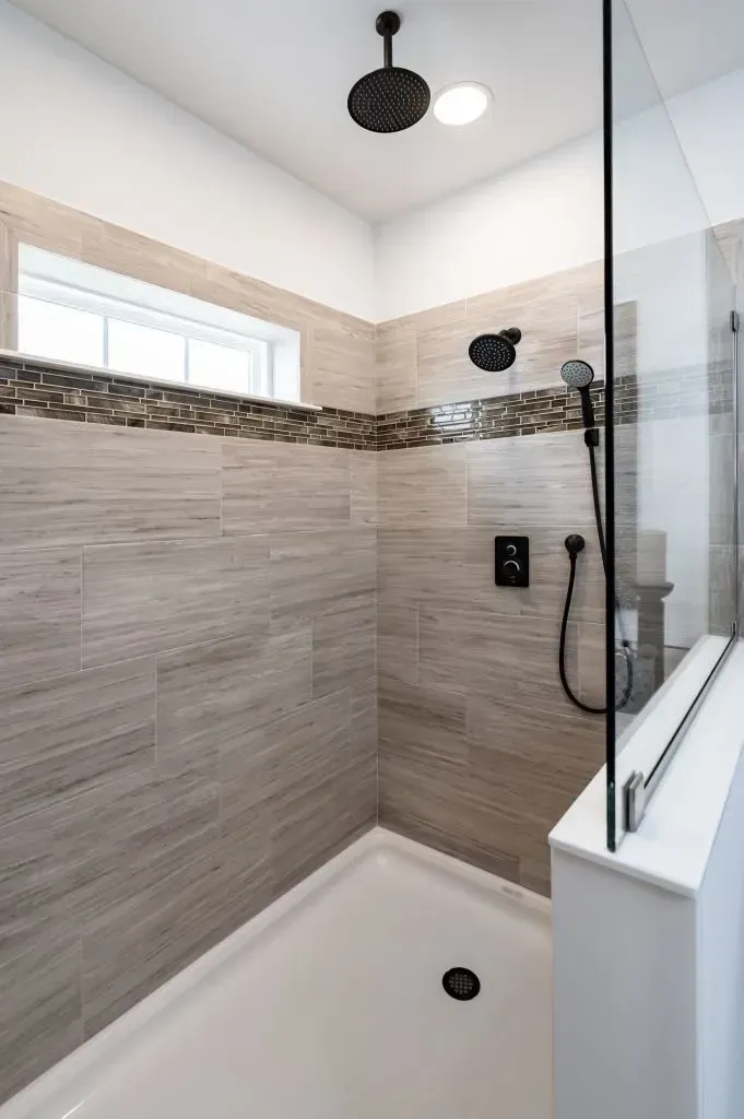 Shower with glass door, light-colored tile walls, black shower fixtures, and a white shower pan.