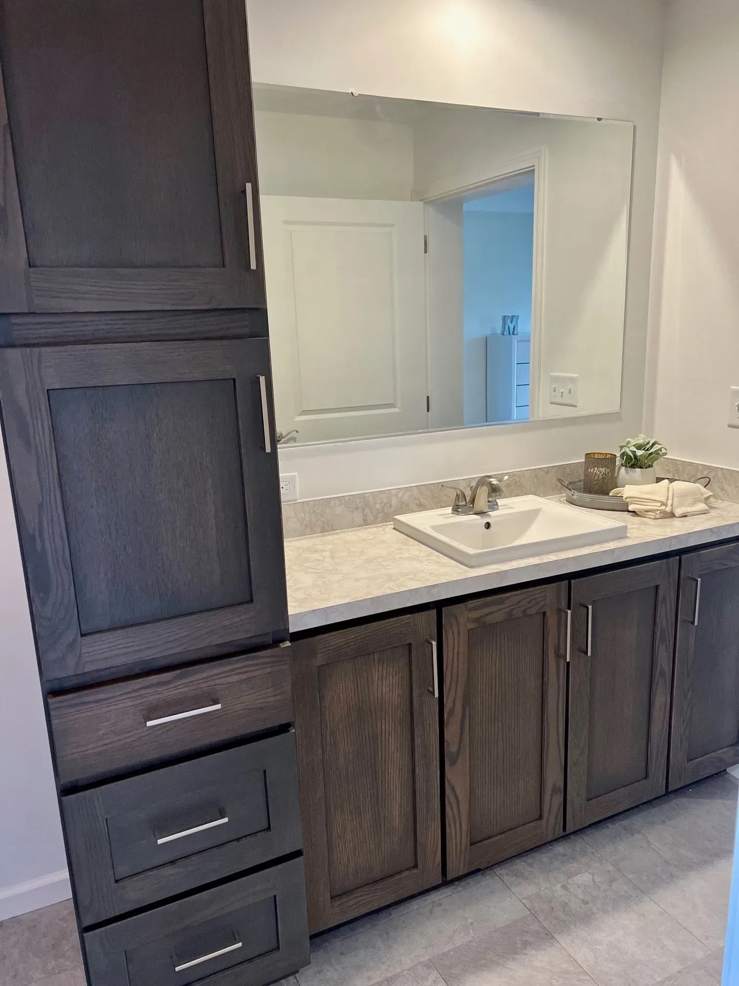 Bathroom with dark wood cabinets, a white countertop, and a large mirror.