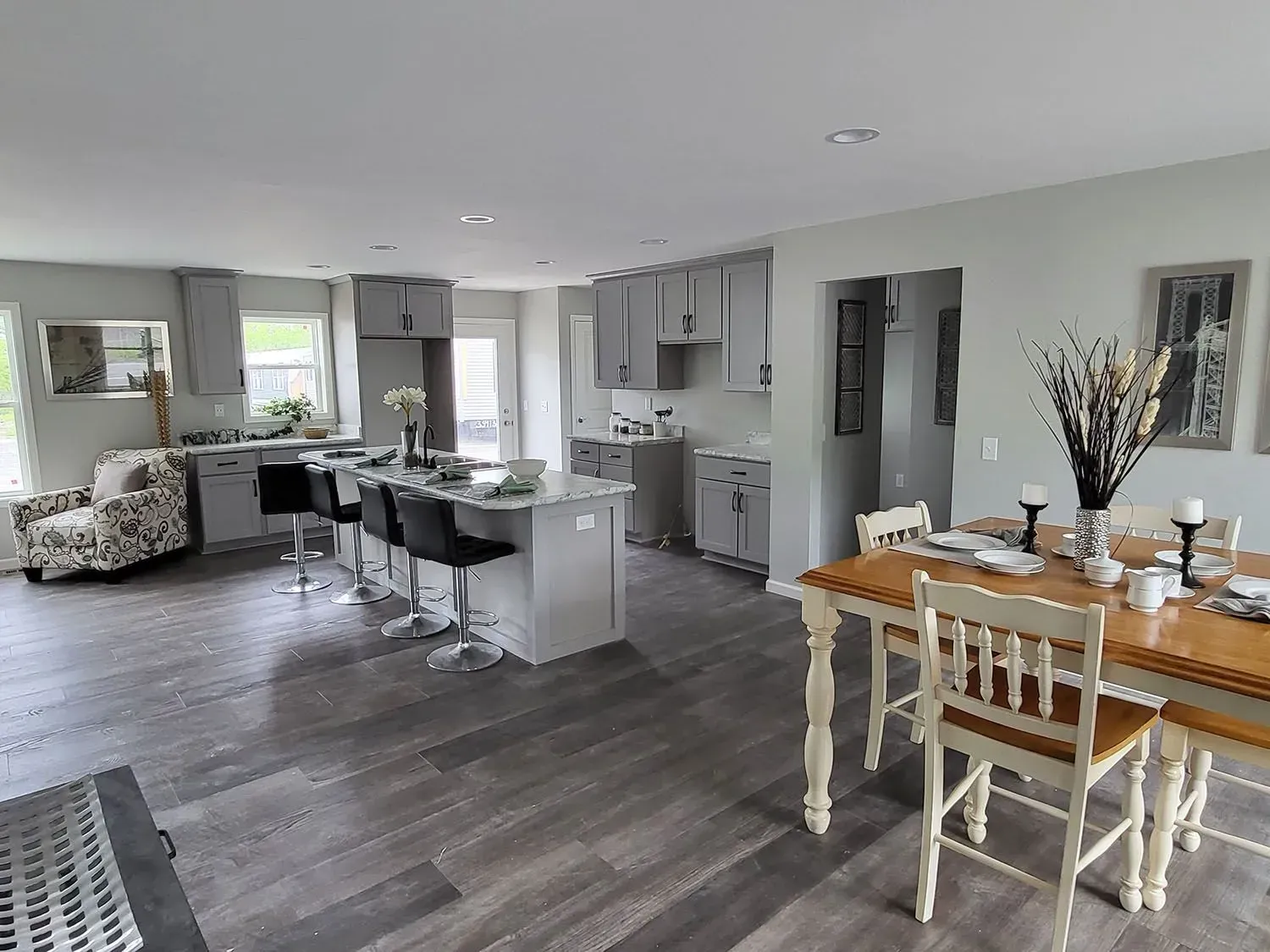 Open-concept kitchen and dining area with gray cabinets, island, and wood-look flooring. Dining table is set.