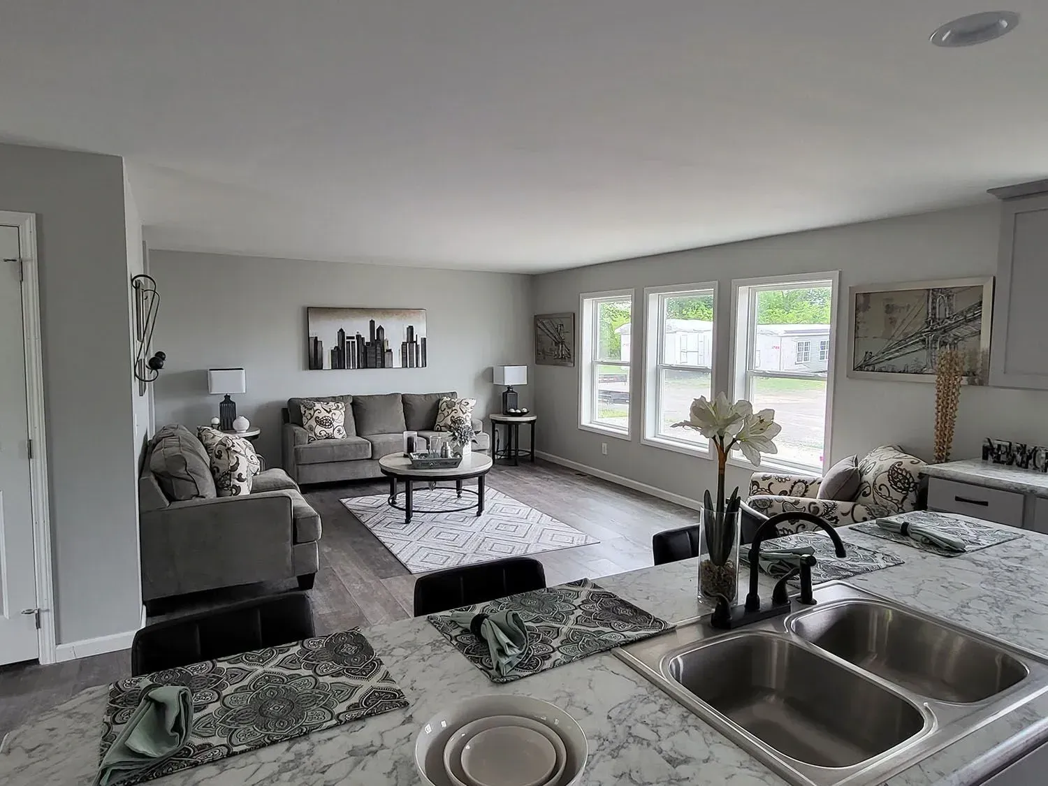 Open-concept living space with a gray sofa, kitchen island with sink, and large windows.