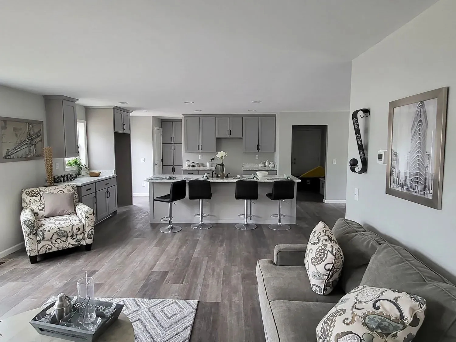 Open-concept living space with gray cabinetry, kitchen island with stools, and gray sofa, hardwood floors.