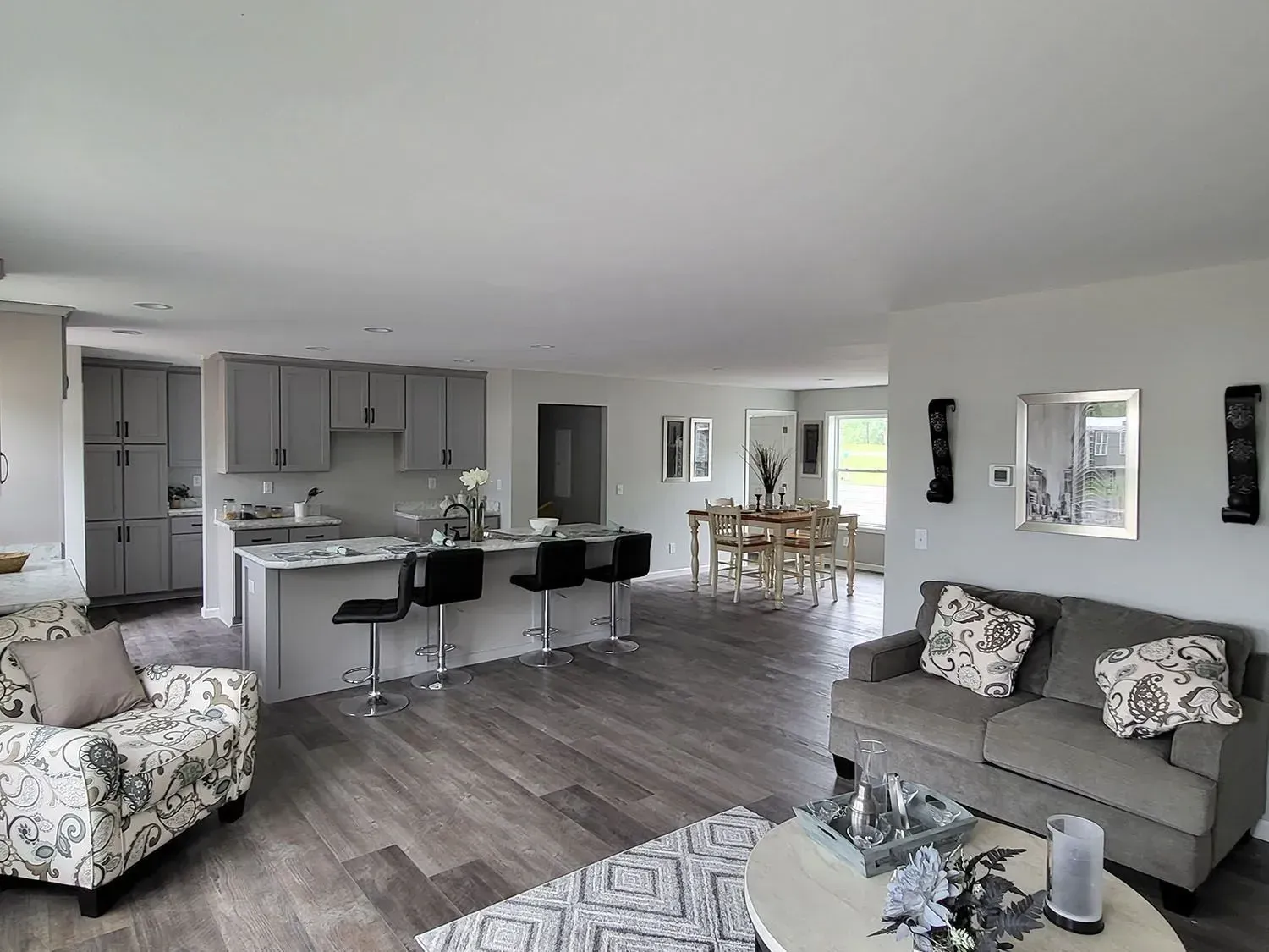 Open-concept living space with kitchen island, seating, and dining area. Gray cabinets, hardwood floors, neutral colors.