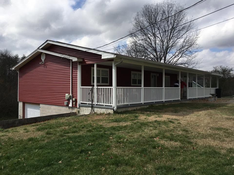 Red house with white porch railing on a grassy hillside under cloudy sky