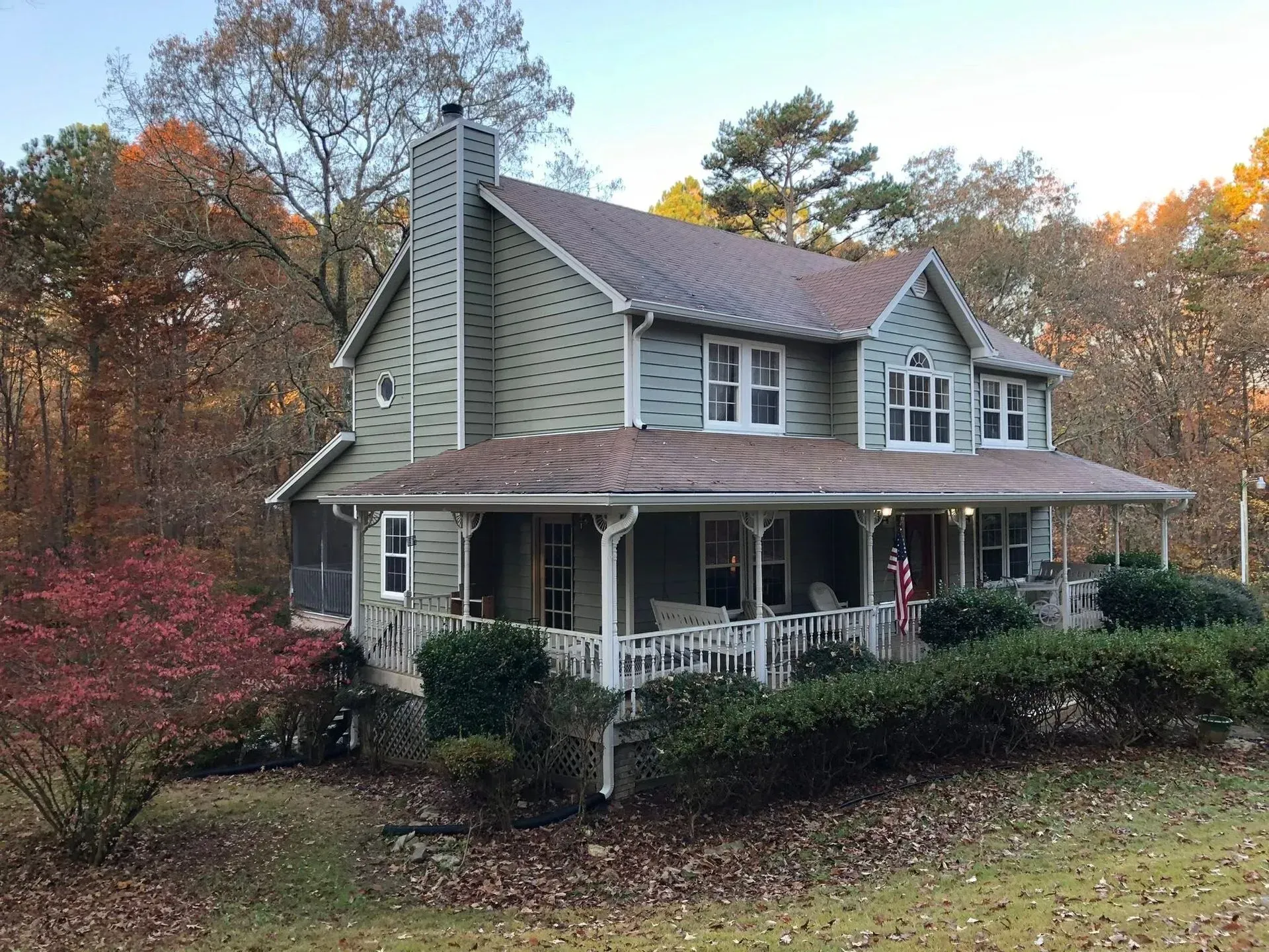 Two-story gray house with a porch, set among autumn trees and shrubs.