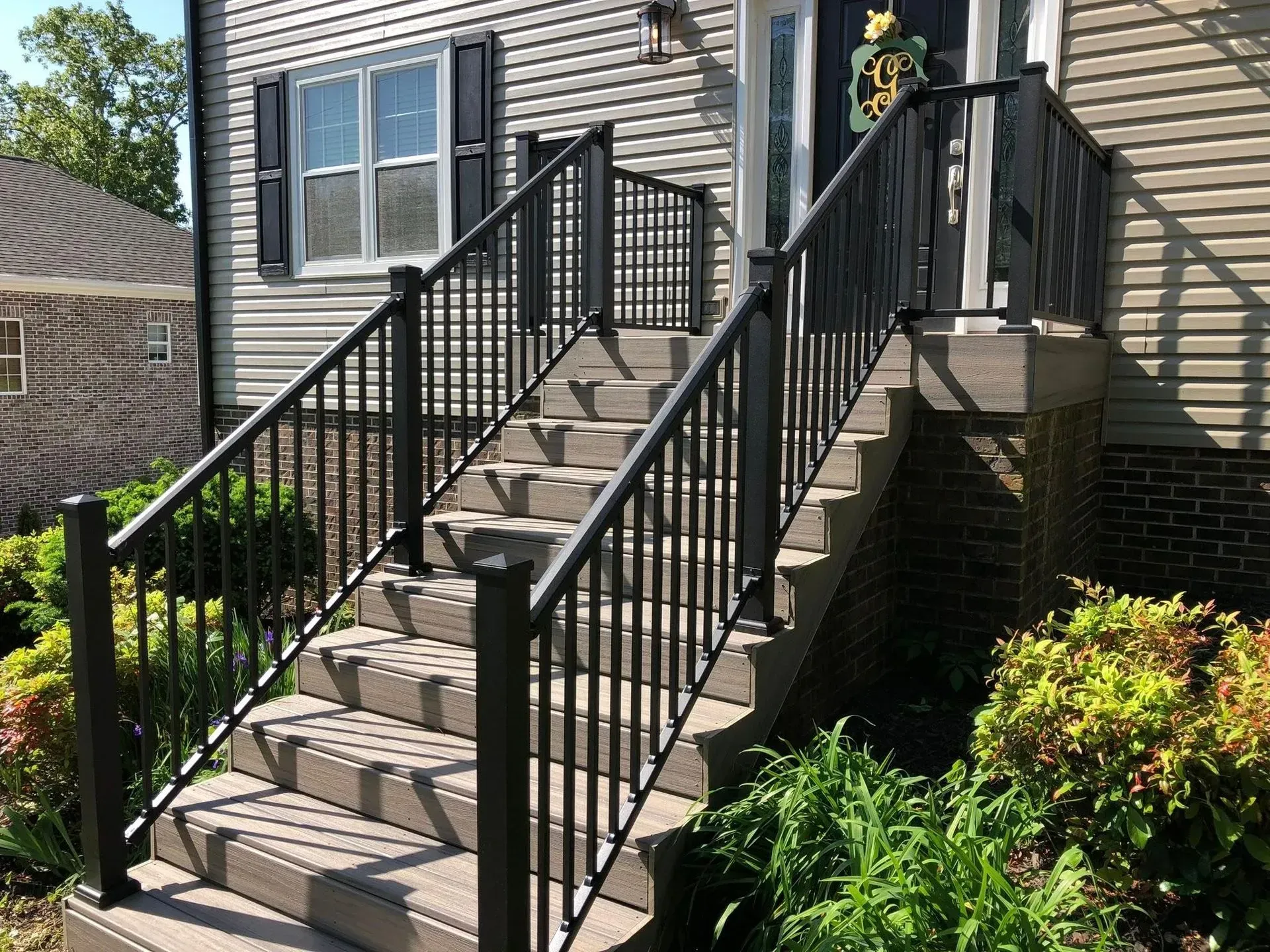 Exterior staircase with black railings leading to a house entrance beside shrubs.