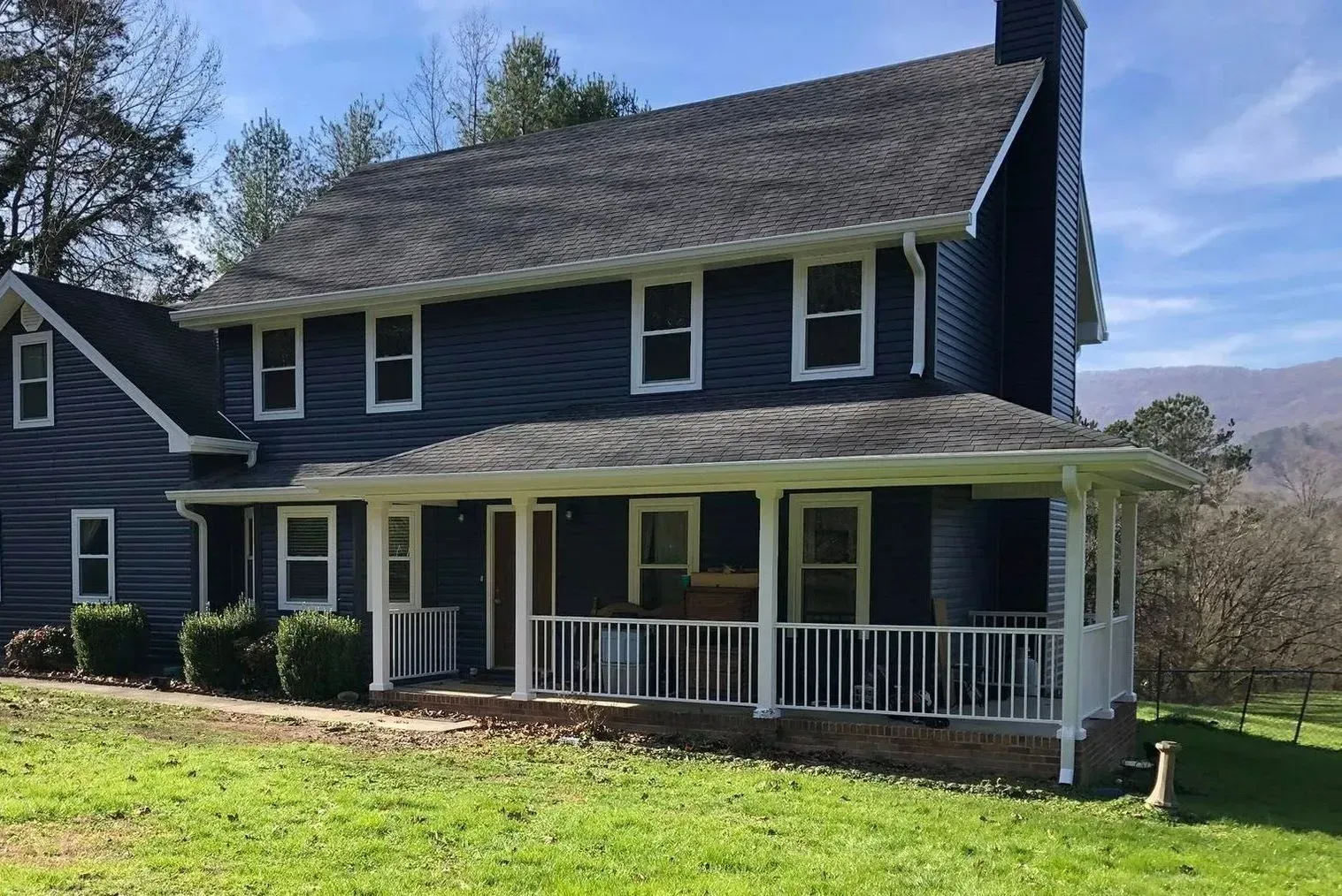 Blue two-story house with white trim and a wraparound porch on a sunny hillside