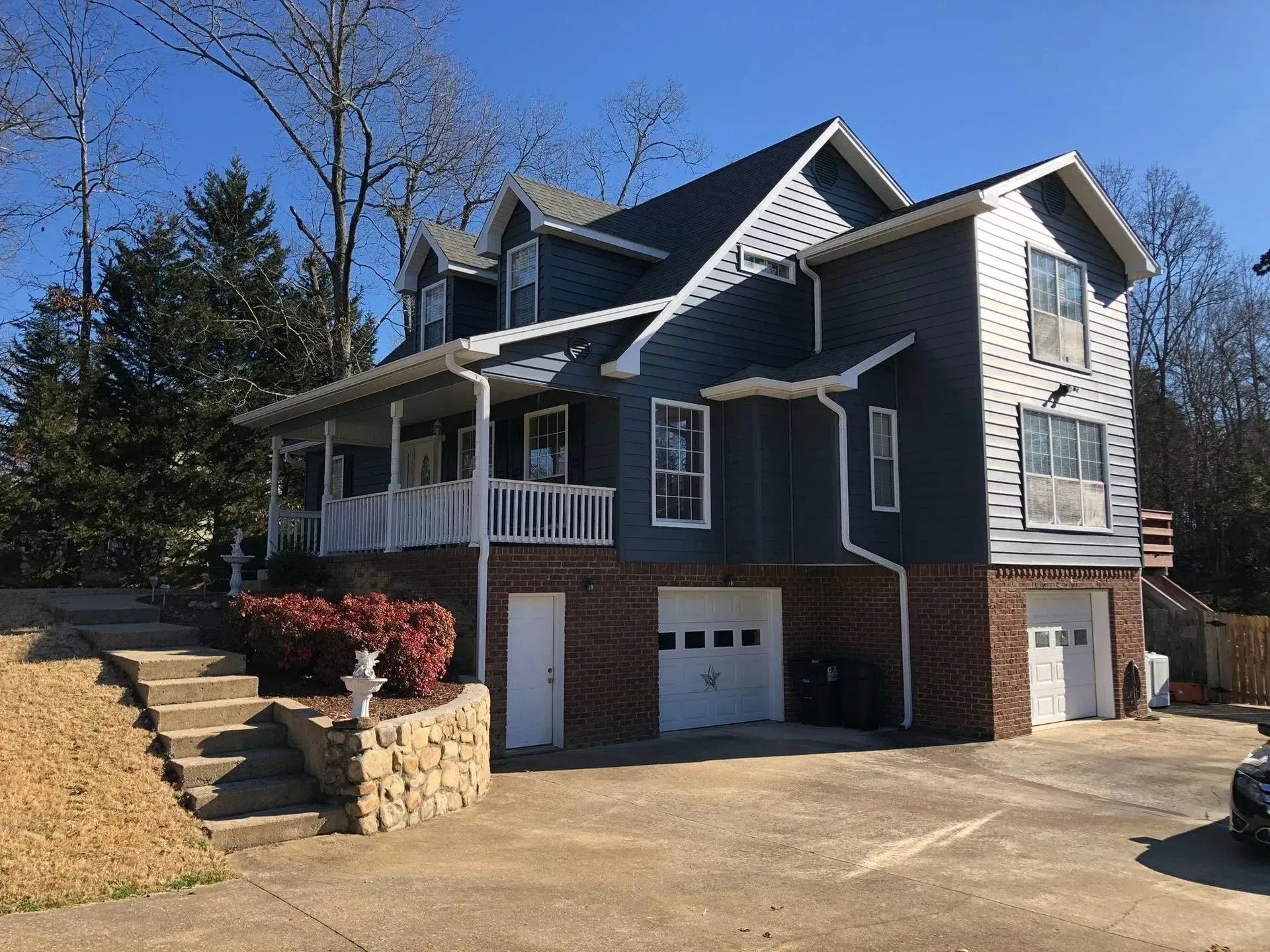 Blue-gray two-story house with white trim, brick lower level, and a driveway in front