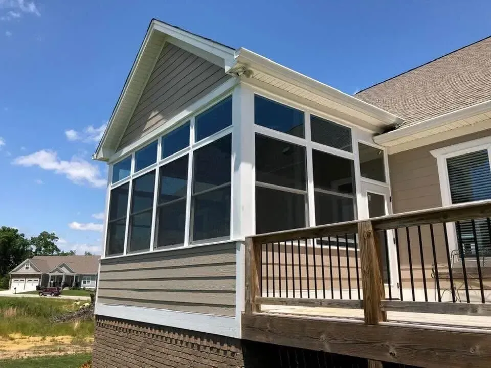 Screened porch with beige siding, white trim, and a wooden railing under a blue sky.