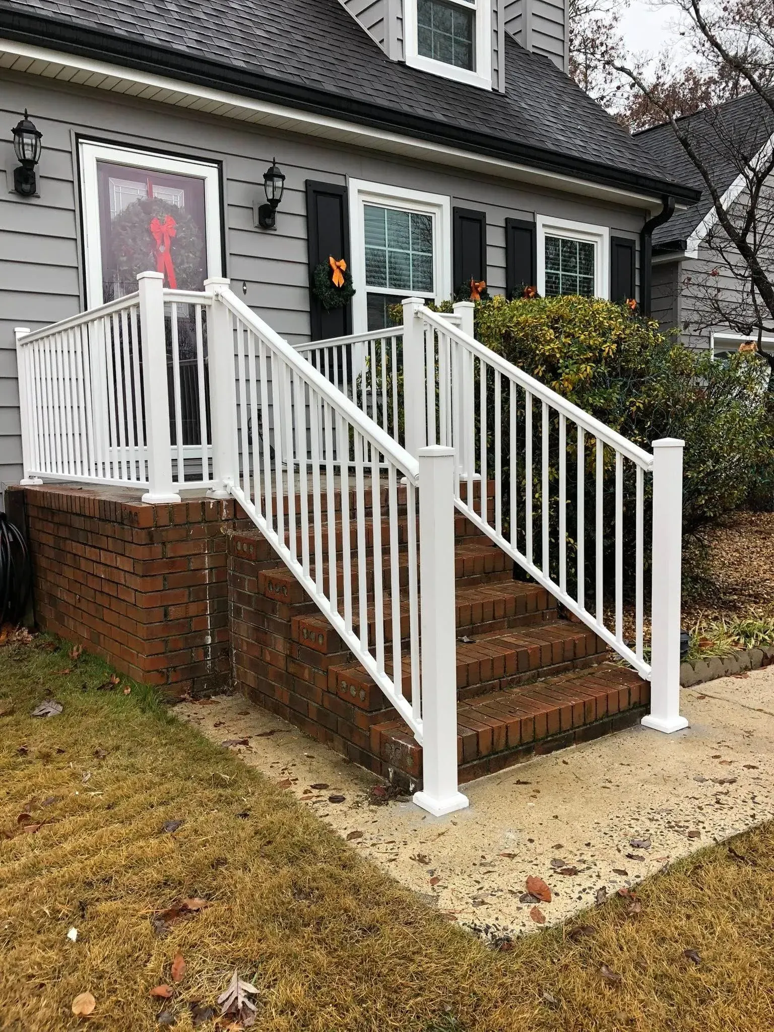 Front porch with brick steps, white railings, and a gray door on a gray house.