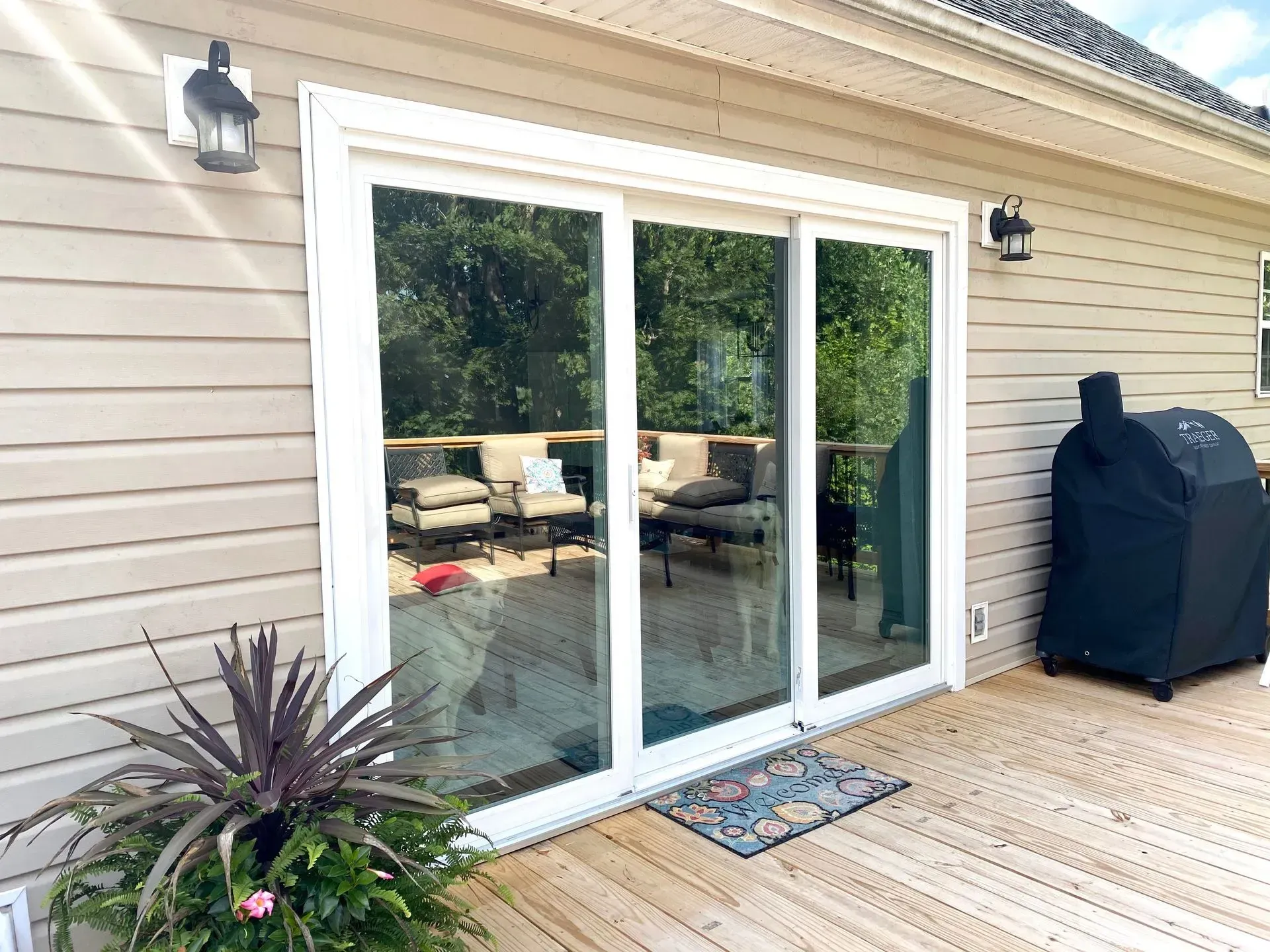 Back patio with sliding glass door, beige siding, potted plant, outdoor rug, and covered grill