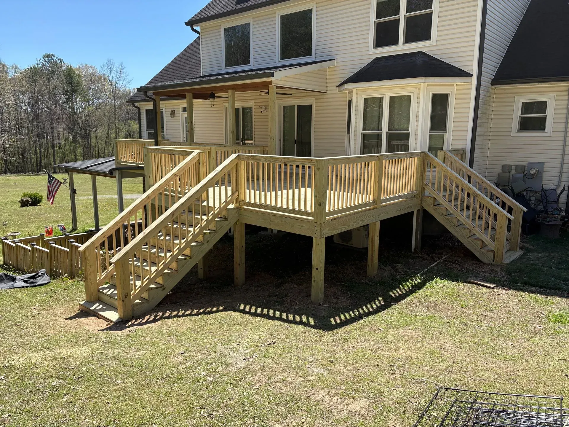 Backyard wooden deck with stairs around a beige house on a sunny day