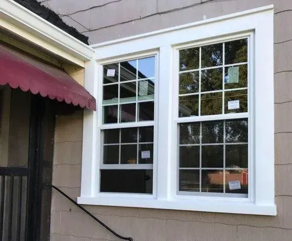 White-framed double window on a tan exterior wall beside a burgundy awning