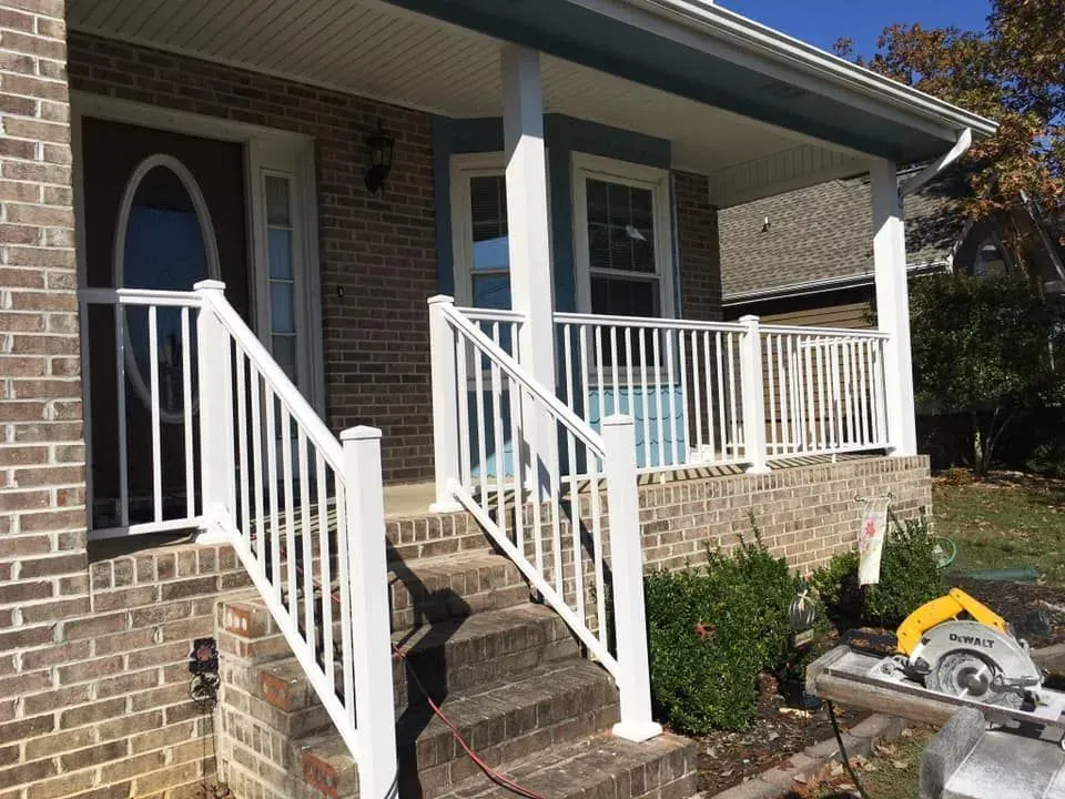 Brick house front porch with white railings and steps, featuring a concrete walkway and a yellow miter saw on the right.