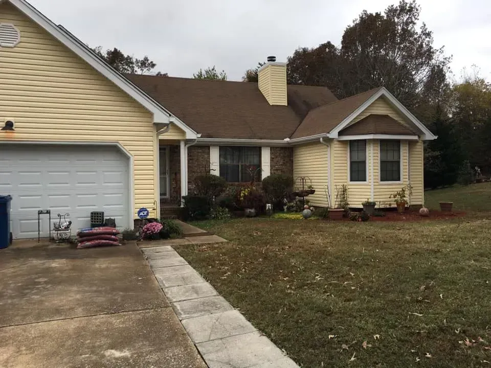 Suburban brick house with yellow siding, garage, driveway, and leafless front yard.