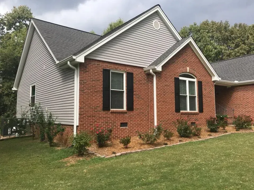 Brick-and-siding suburban house with dark shutters and a grassy front yard
