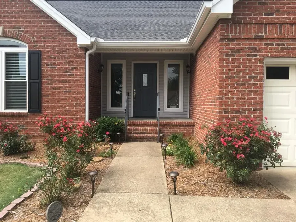Brick house front entrance with concrete walkway, red rose bushes, and a white garage door