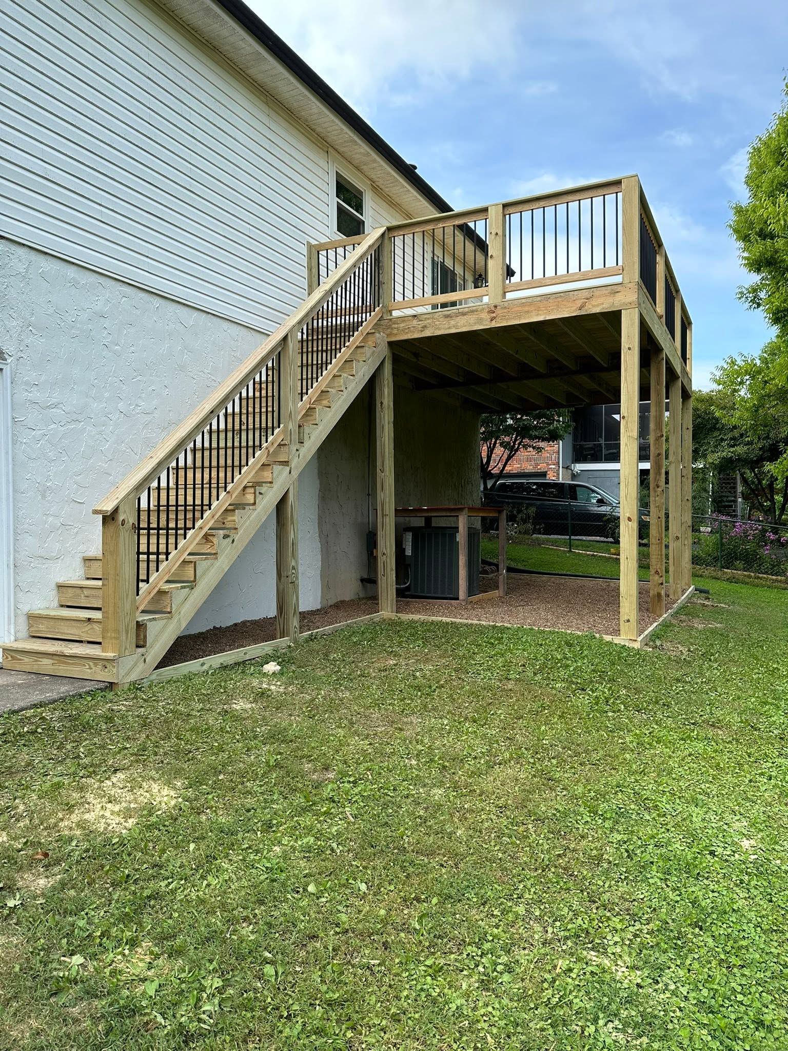 Wooden outdoor staircase and raised deck beside a white building, overlooking a grassy yard.