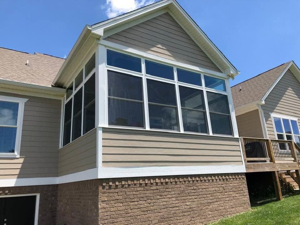 Screened sunroom on a beige house with white trim and stone foundation under a blue sky