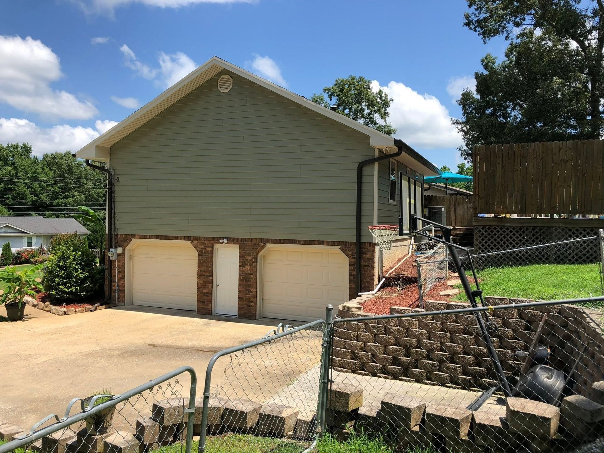 House with detached garage, sloped driveway, stone retaining wall, and a fenced yard on a sunny day