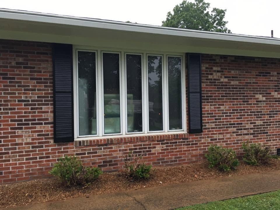Brick house exterior with a white-trimmed window and shrubs beneath a covered roofline