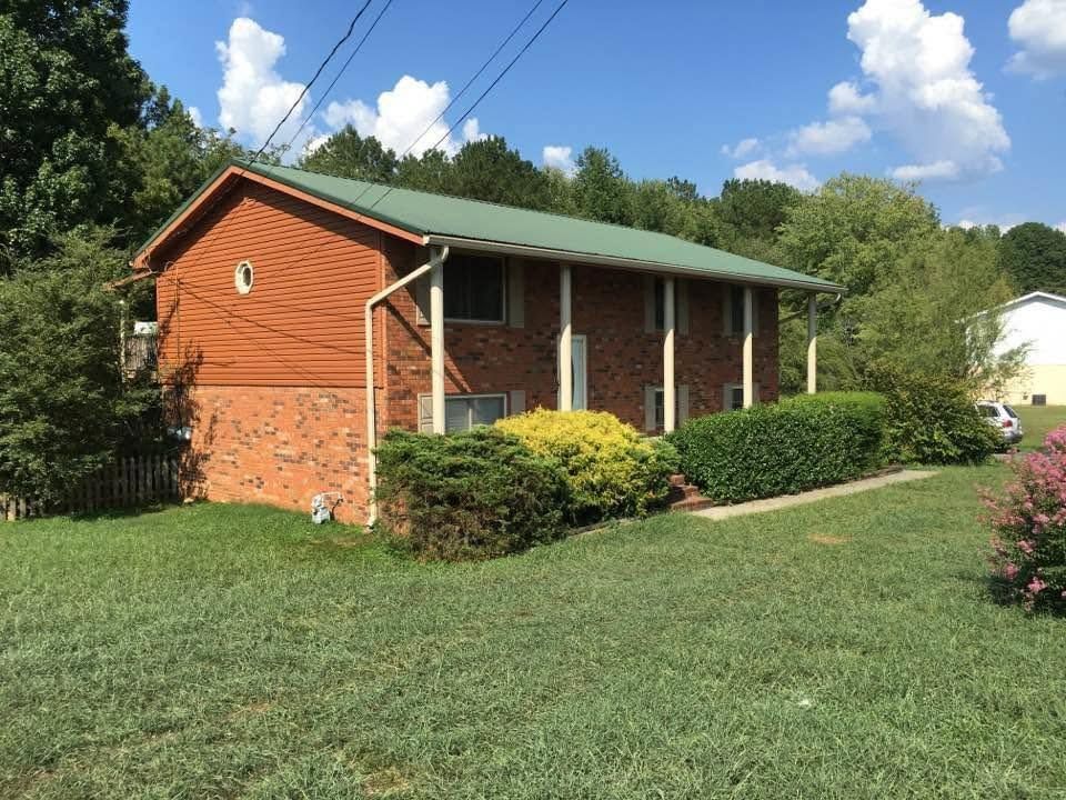 Small brick house with a green roof and trimmed bushes on a sunny lawn