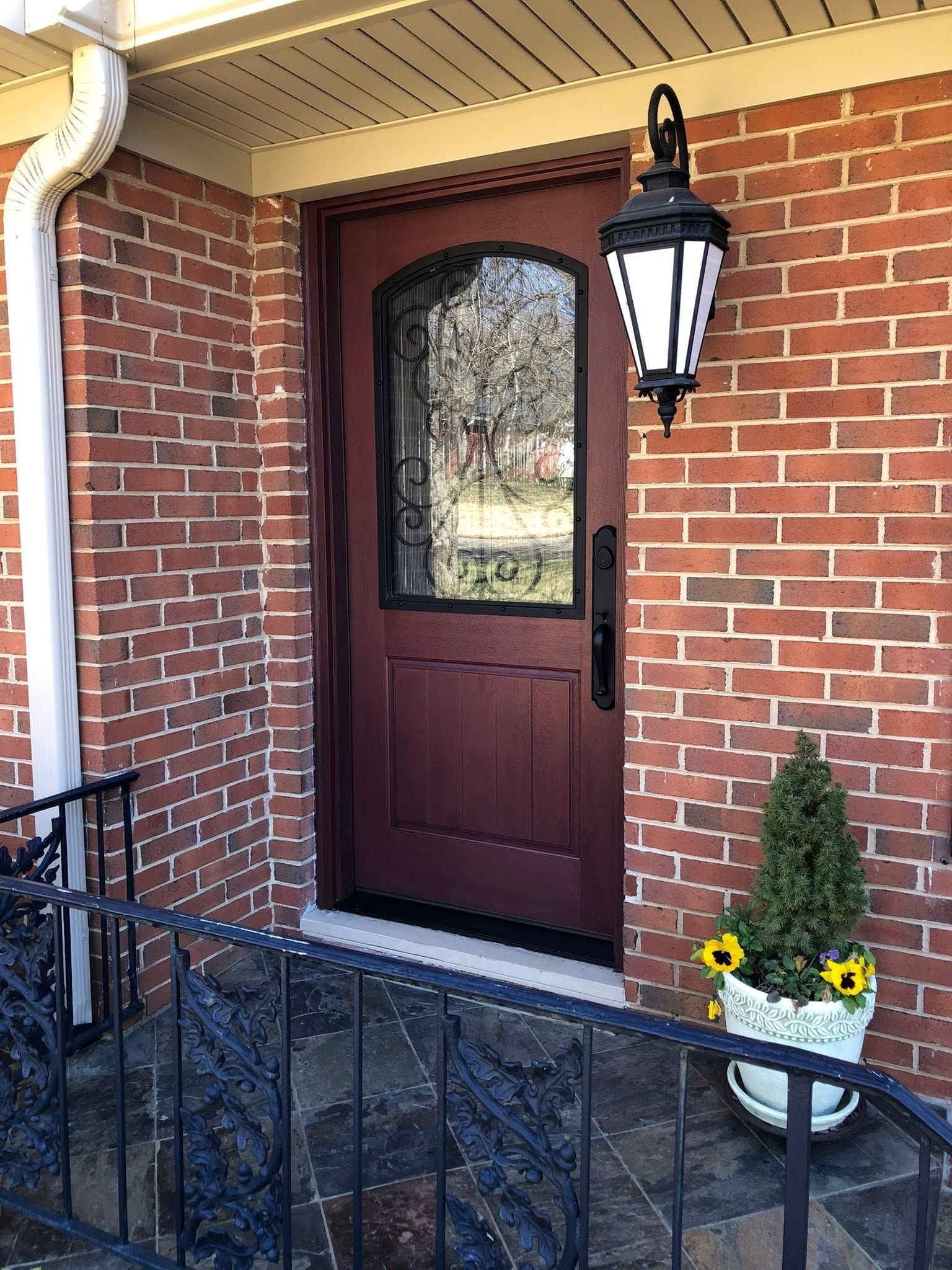 Brick front porch with a dark wooden door, black lantern, and potted flowers by the entrance