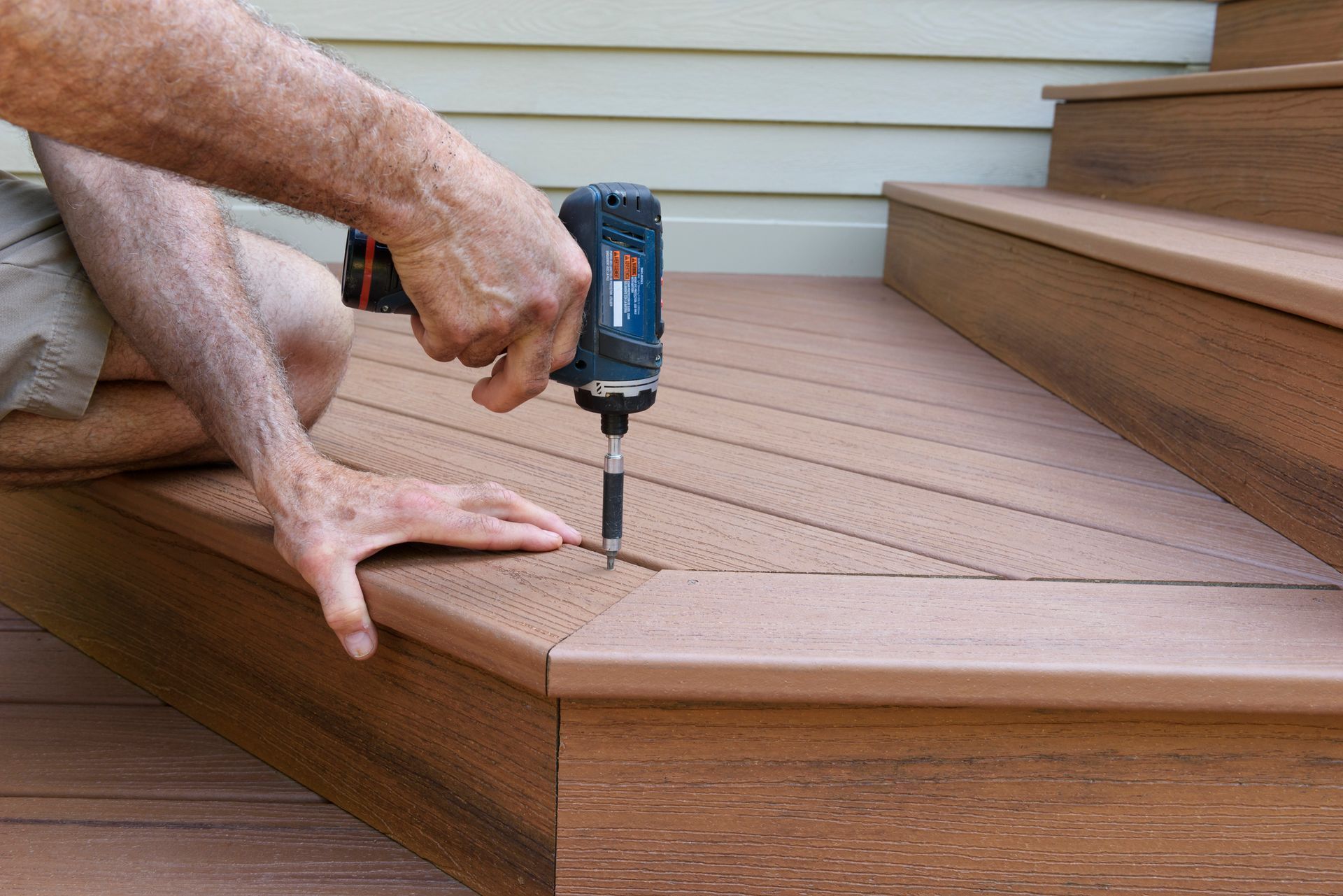 Person using a drill to fasten deck boards on a wooden porch step