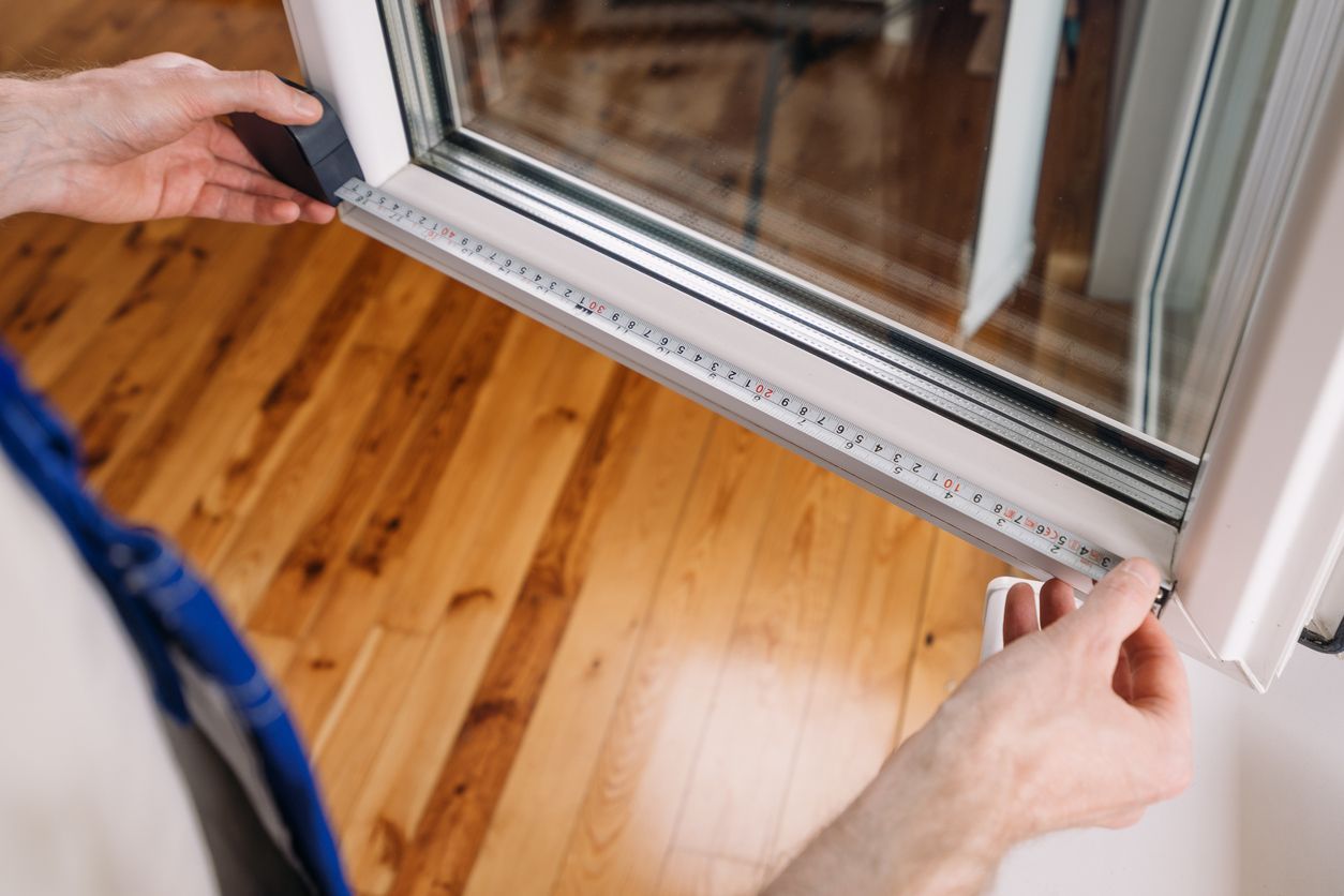 Hands measuring a sliding glass door frame with a tape measure over a wooden floor