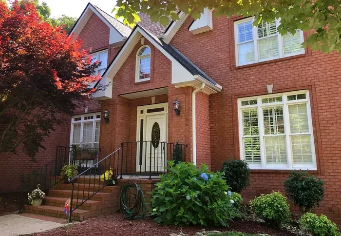 Brick house with white trim, front porch, and landscaped garden under red-leafed trees