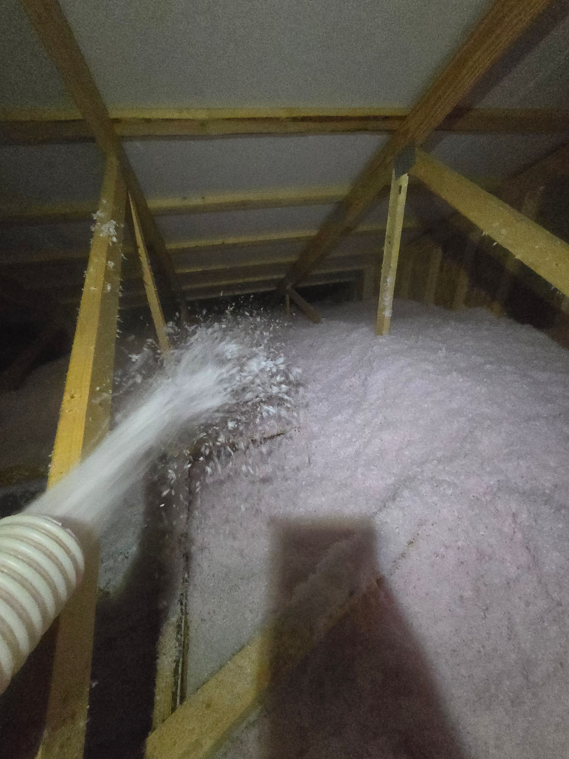 A person is blowing insulation into an attic with a hose.
