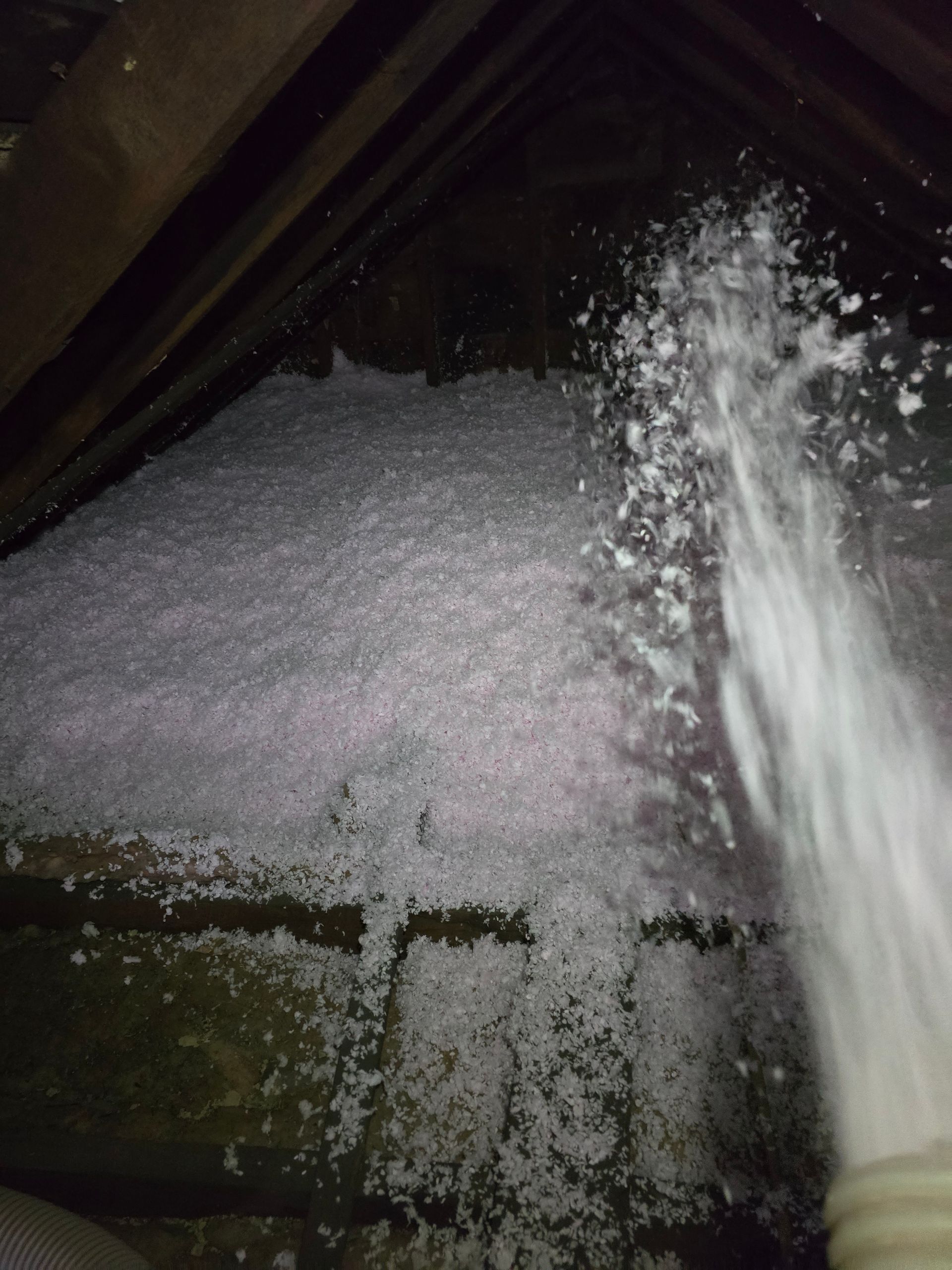 A person is spraying water on a pile of insulation in an attic.