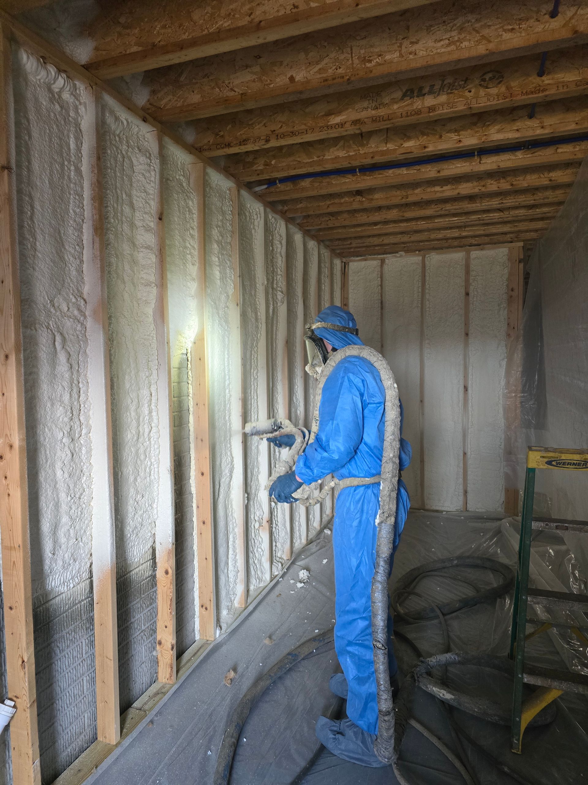 A man in a blue suit is spraying foam on a wall.