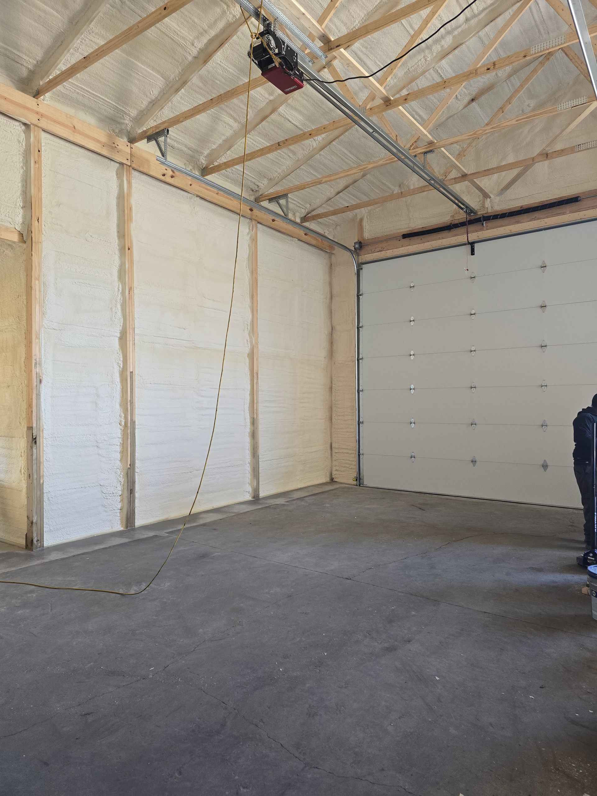 A man is standing in an empty garage with a garage door open.