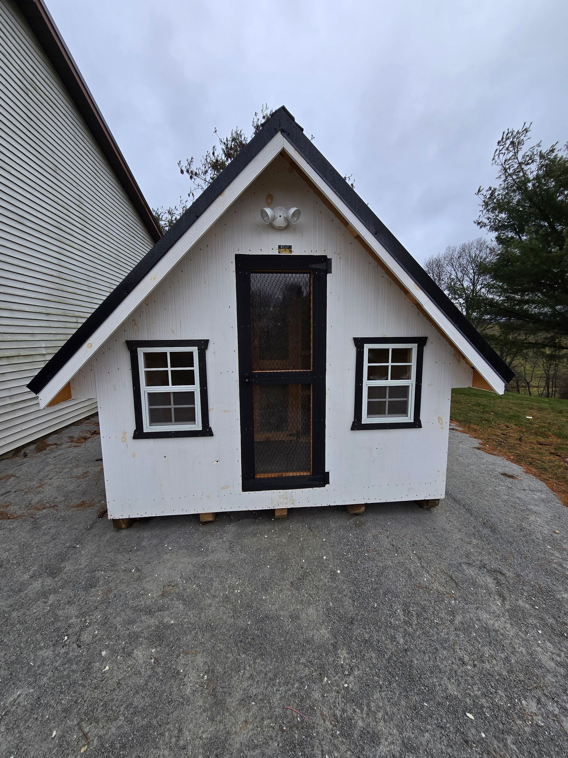 A small white house with black trim and windows is sitting on a gravel road.
