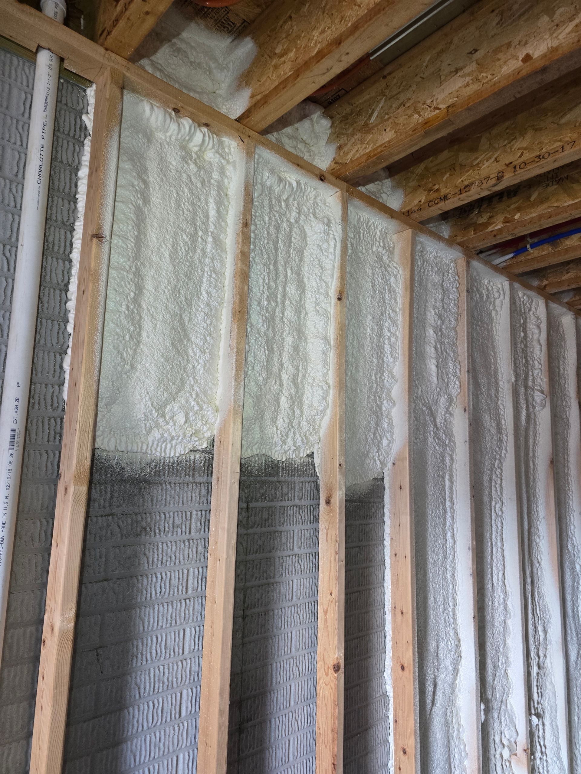 A wall is being insulated with spray foam and wooden beams.